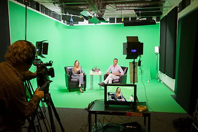 Woman and man sitting in front of a green screen.